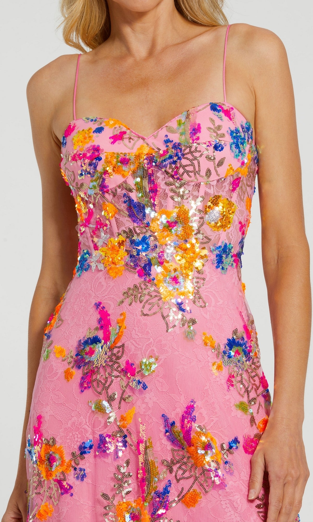 A woman wears the Long Formal Dress 68508 by Mac Duggal, a pink sequin floral gown with a sweetheart neckline and colorful embroidered embellishments.
